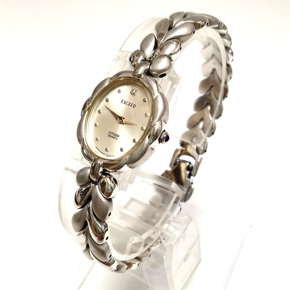 CITIZEN Exceed SV925 silver ladies wristwatch with oval dial and decorative silver bracelet shown on a clear display stand.