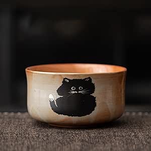 Ceramic matcha/rice bowl with a black cat illustration on the exterior, shown on a textured surface.