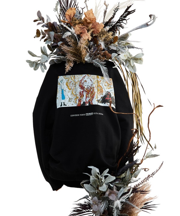 Back view of a black cotton T-shirt showing a rectangular silk-screen art print on the back alongside a dried floral arrangement.