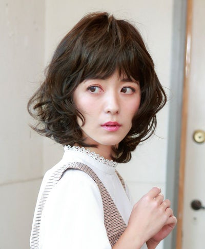 Model wearing a brown retro bob all-wig (synthetic) with layered wavy curls and bangs, shown from the side.