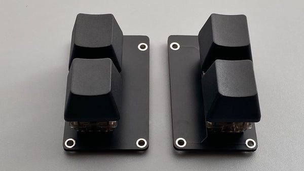 Two black key expansion plates for claw44v3/wings42 shown with two keycaps mounted on each plate.