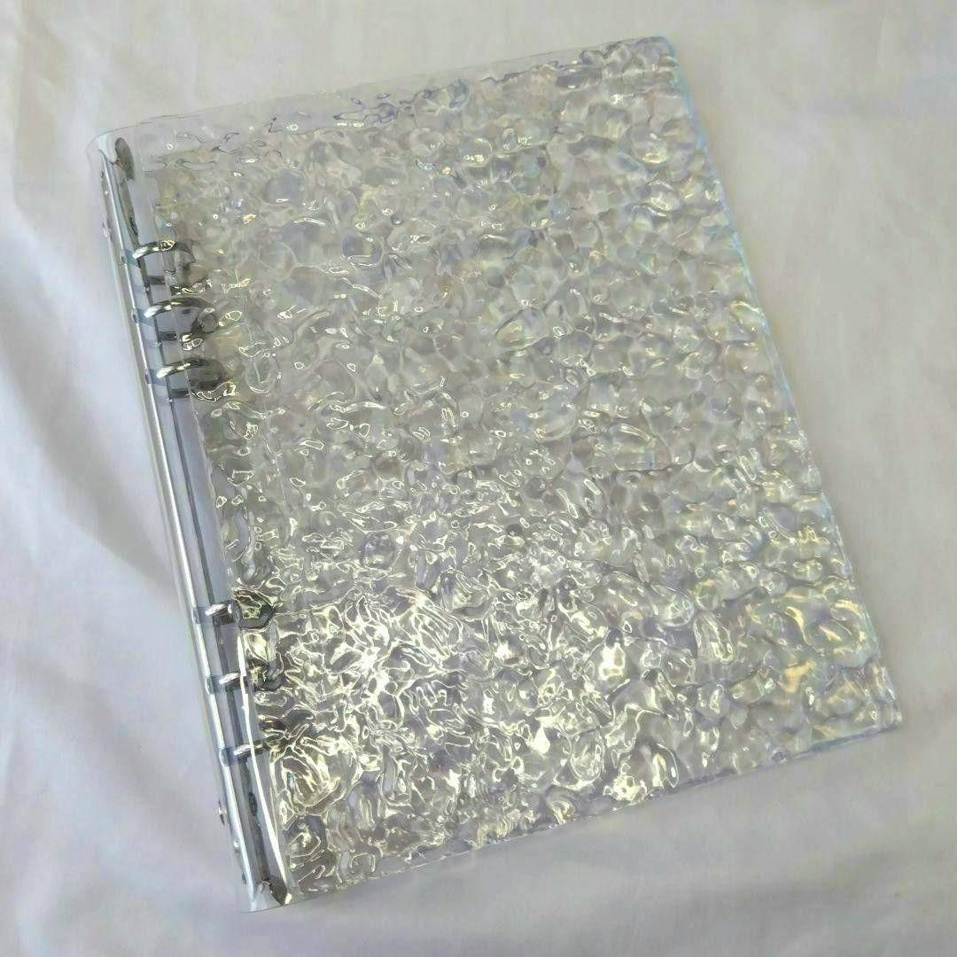 Clear textured acrylic binder showing the front cover and visible metal ring spine on a white background.