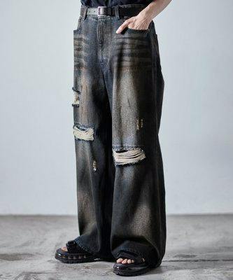 Model wearing men's wide-leg dark-wash distressed denim jeans with frayed knee damage, shown from the front.