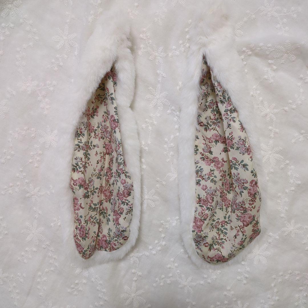Pair of white faux-fur bunny-ear ear warmers with floral patterned inner lining laid flat on fabric.