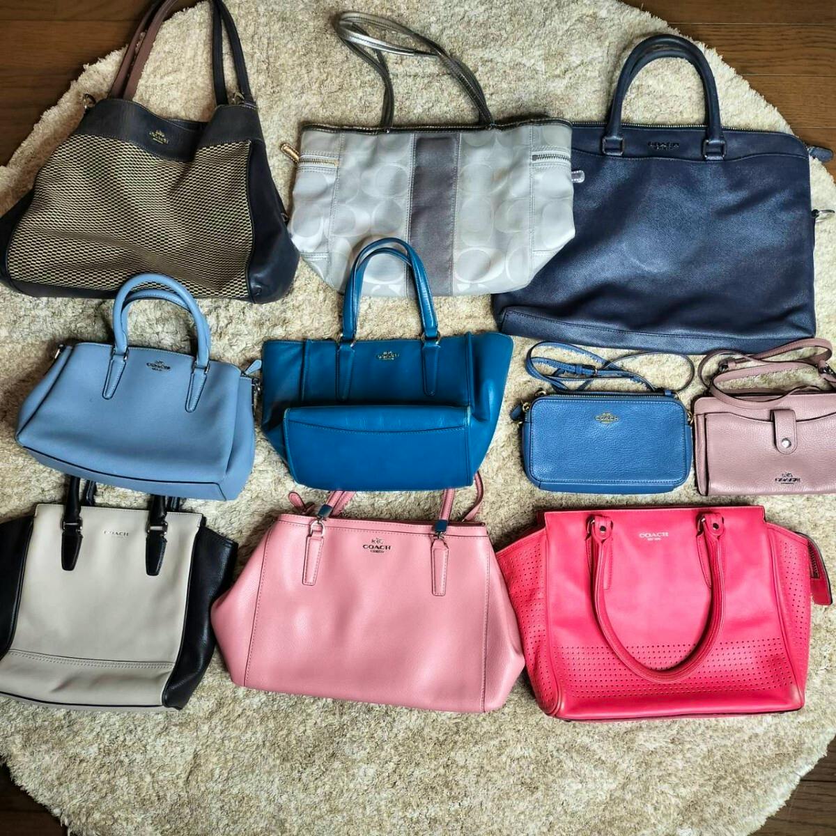 Multiple COACH leather handbags and small wallets in assorted colors arranged on a carpet.