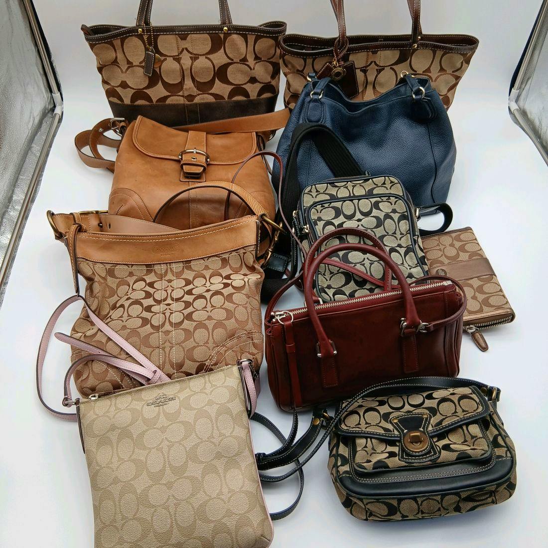 Multiple Coach bags and wallets arranged on a white background, showing signature C canvas and leather pieces.