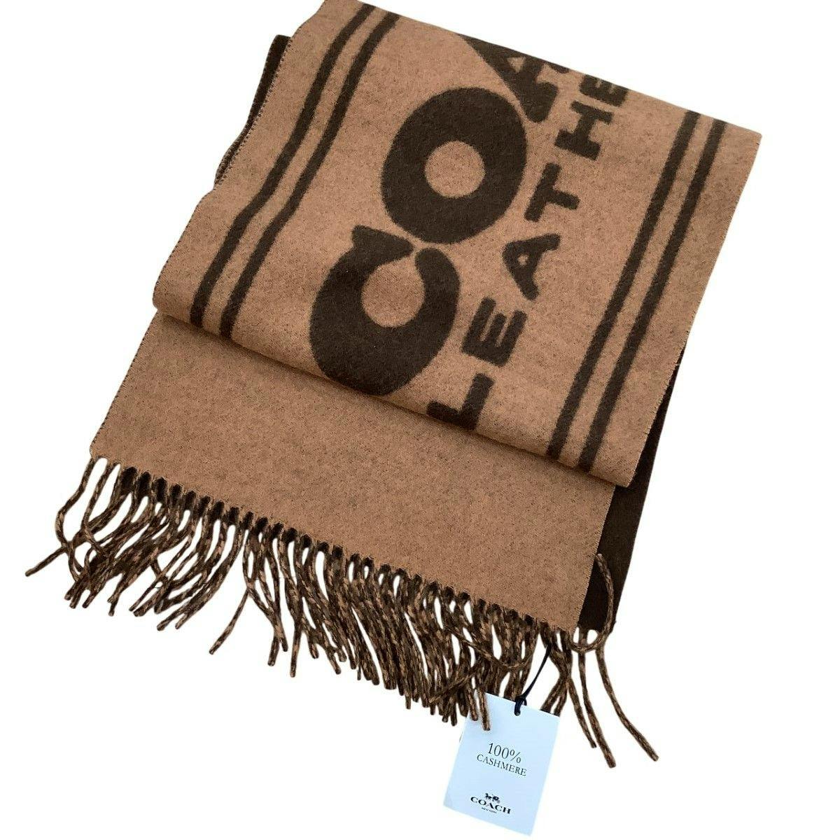 Folded brown COACH 100% cashmere muffler with fringe and a tag reading “100% CASHMERE”.
