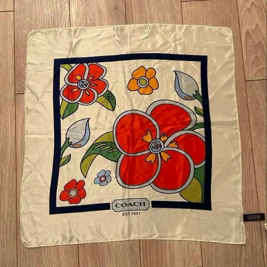 A 53 cm square silk COACH scarf laid flat on a wooden floor showing a large red floral print and the COACH logo.
