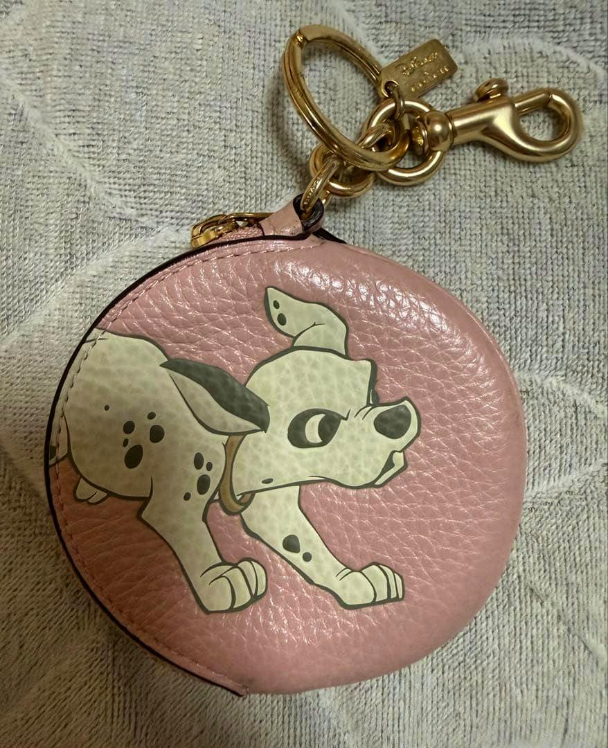 Front view of a round pink COACH coin case with a 101 Dalmatians puppy print and attached gold keychain hardware.