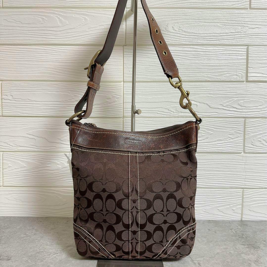 Brown Coach signature canvas shoulder bag with leather trim and adjustable strap hanging on a stand.