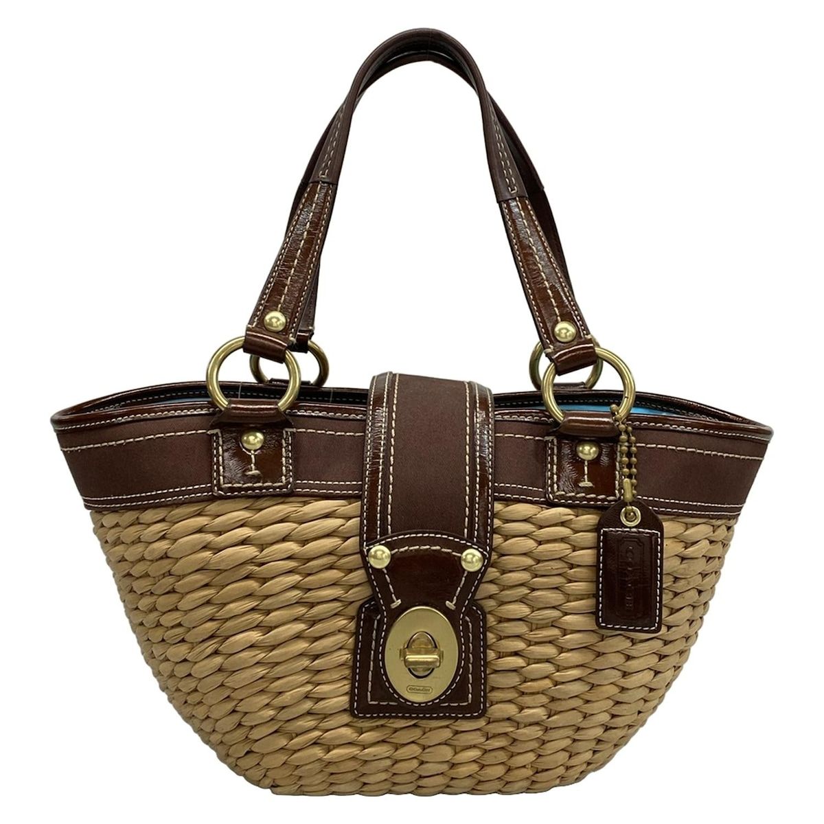 Front view of a COACH beige and dark brown leather basket bag with braided body, leather trim, and a turn-lock clasp.