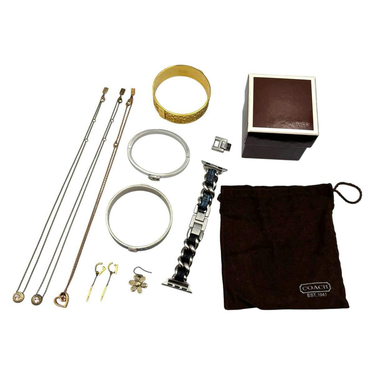 Assorted Coach jewelry and accessories laid on a white background, including necklaces, bracelets/bangles, earrings, a Coach drawstring pouch and a Coach box.