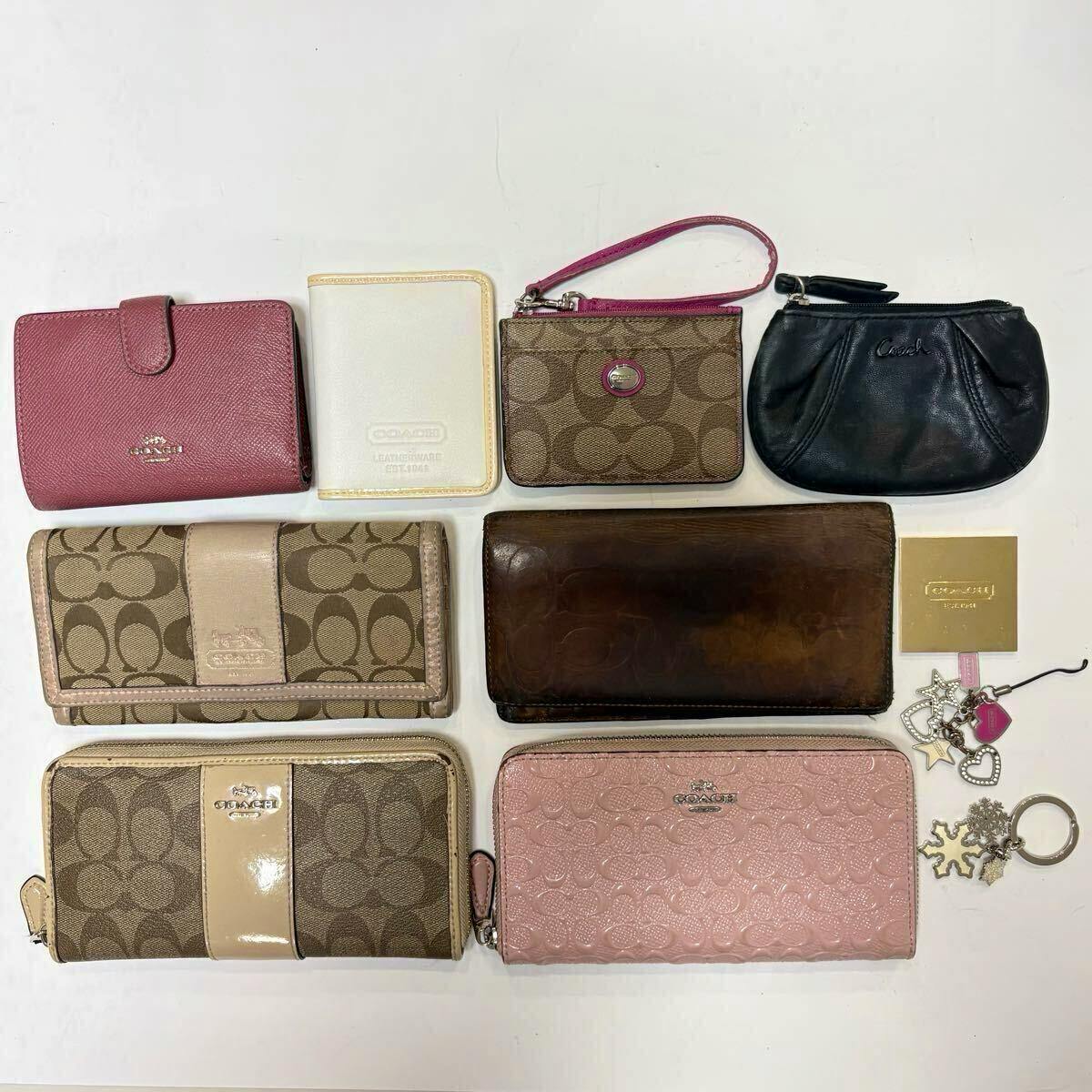 Flat lay of assorted COACH items including wallets, coin cases, pouches, keychains, charms, and a small mirror on a white background.