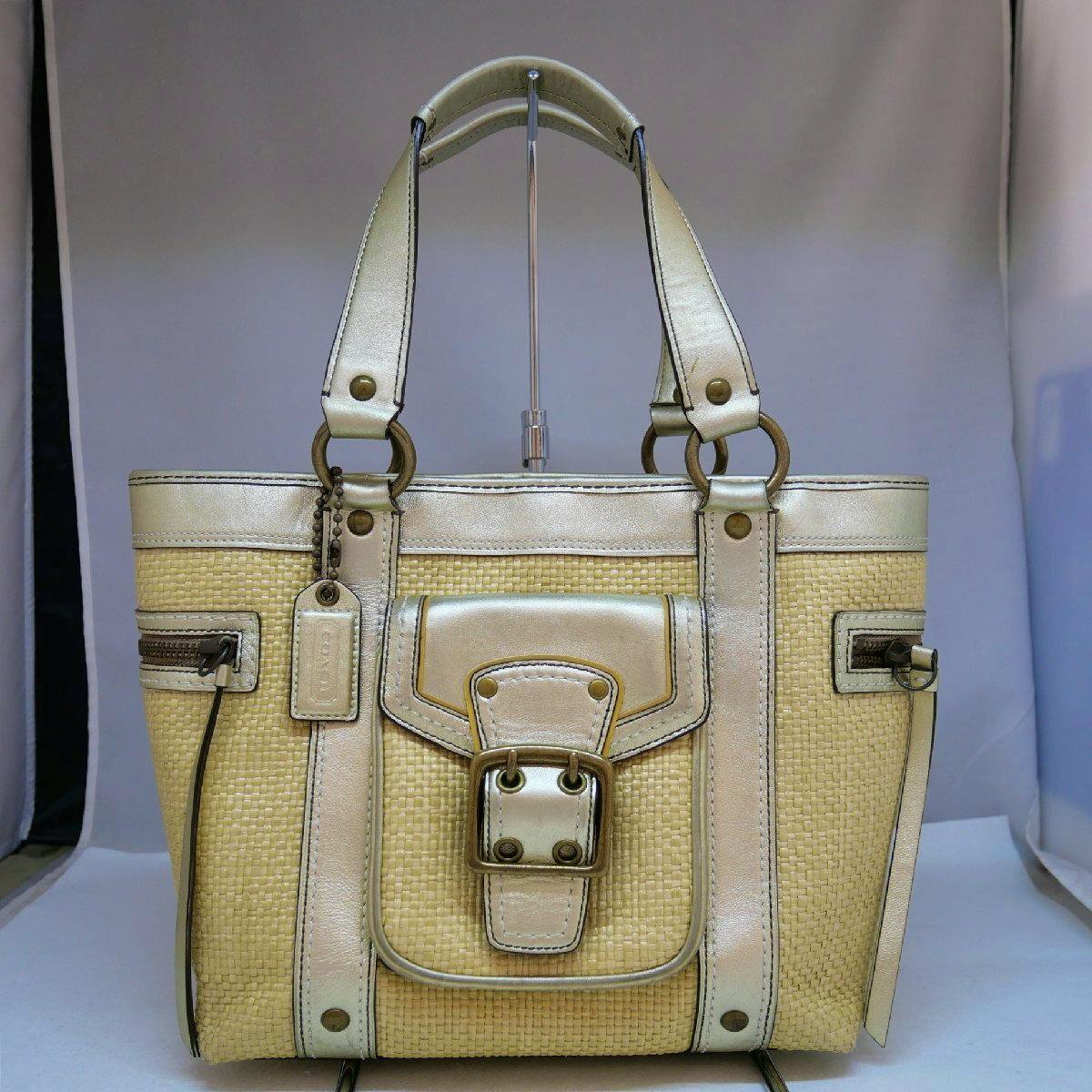Front view of a used COACH beige and white straw woven tote handbag with leather trim, double handles, and front buckle pocket.