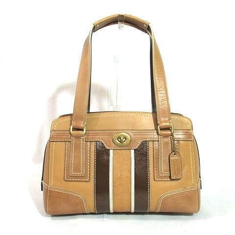 Front view of a beige and brown Coach leather shoulder handbag with turn-lock closure and a logo charm.