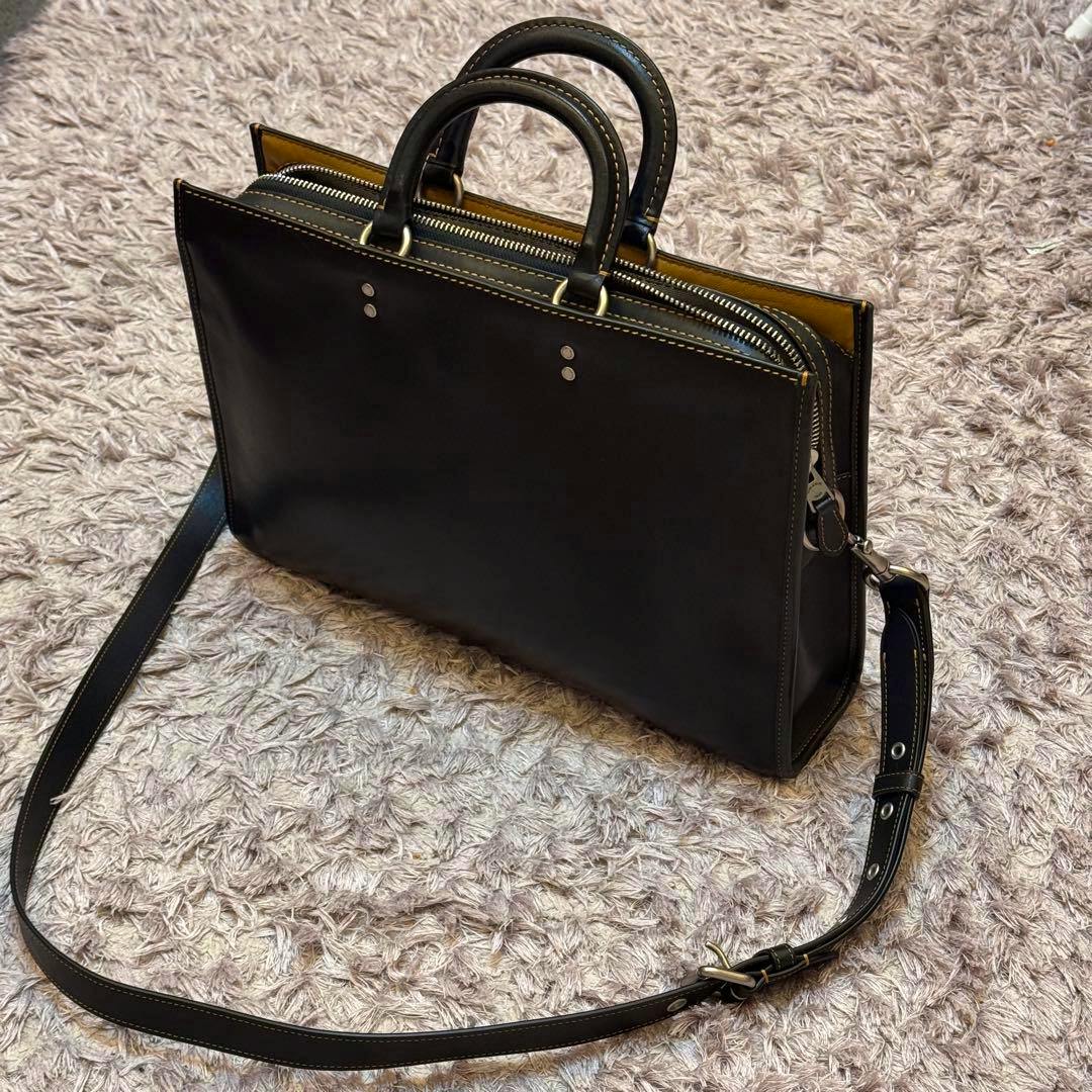 Coach leather 2-way business bag with top handles and an adjustable shoulder strap photographed on a textured rug.