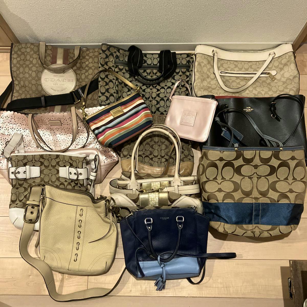 Multiple Coach bags and purses arranged on a wooden floor, featuring signature 'C' canvas patterns, leather, and various styles.