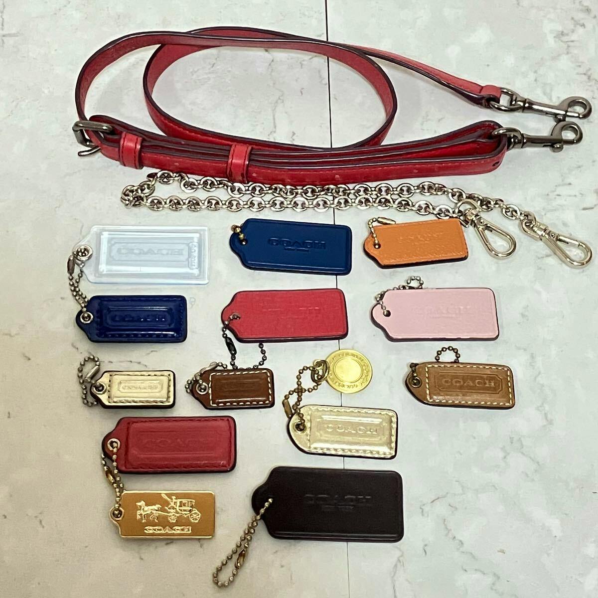 Multiple Coach bag tags, chains, and a red shoulder strap laid flat on a light surface.