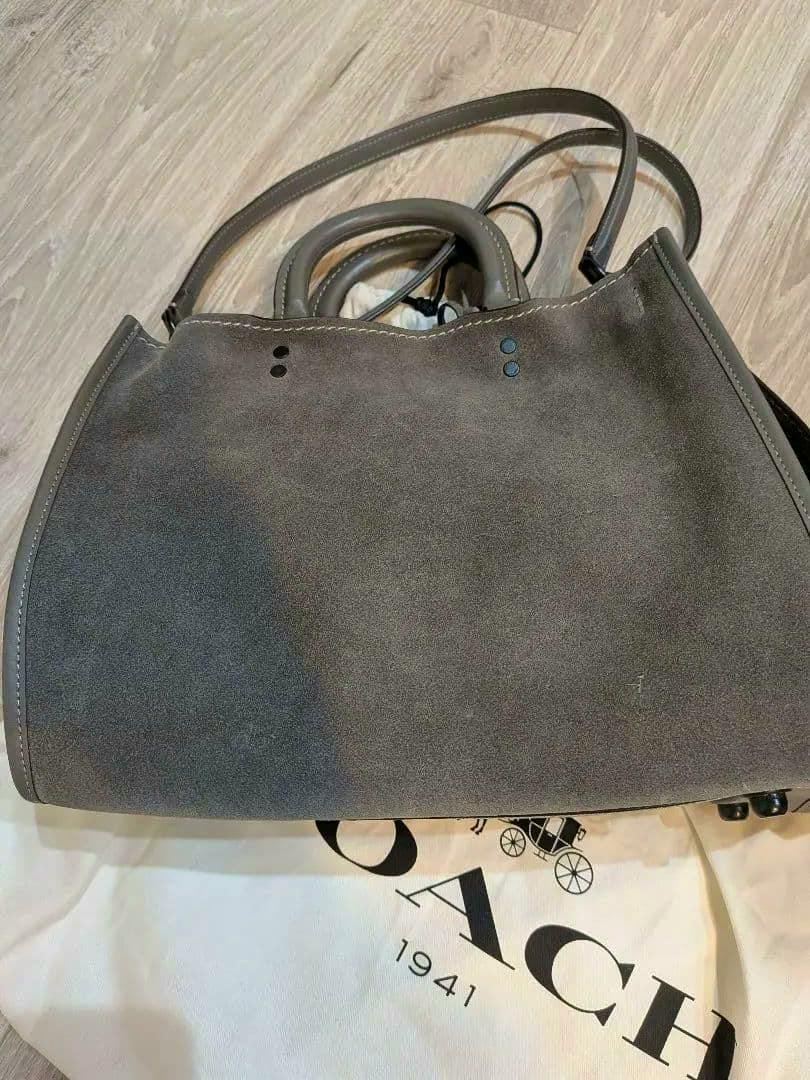 Gray COACH 1941 suede tote bag shown on a COACH dust bag with handles visible.