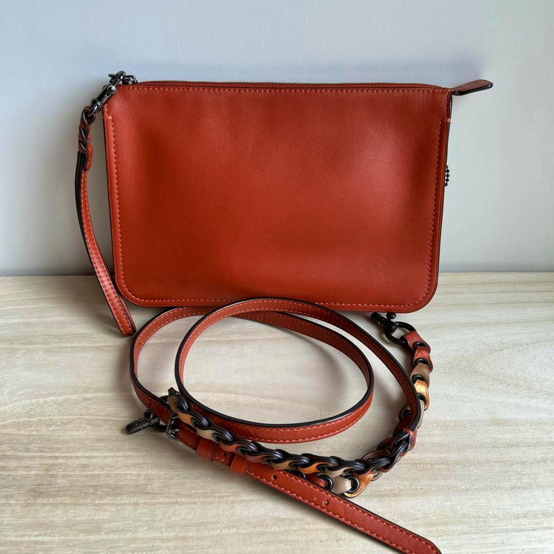 Front view of the Coach 1941 Soho crossbody grab-tan leather bag in orange with its long chain-and-leather strap coiled in front.