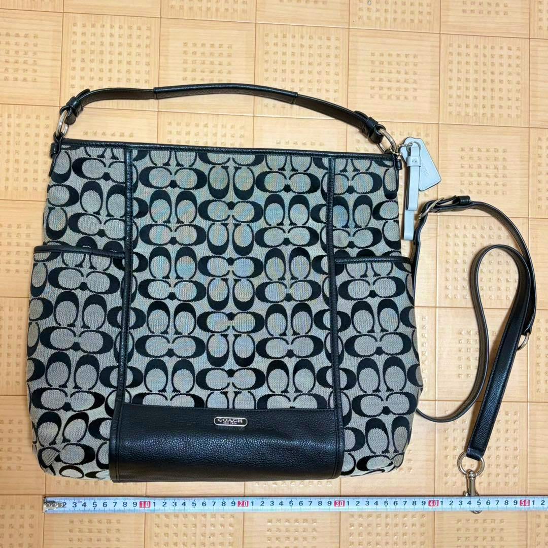 Front view of the Coach canvas 2-way handbag showing the signature C pattern, leather trim, detachable shoulder strap, and a measuring tape at the bottom.