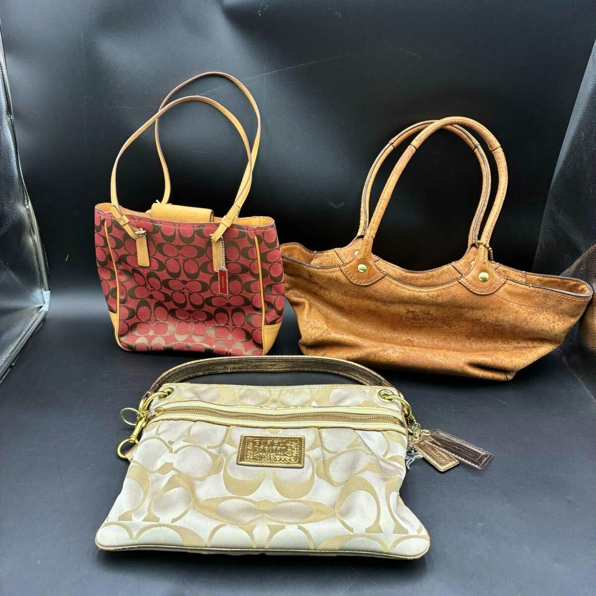 Three COACH bags displayed against a black background: a red monogram tote, a brown leather tote, and a beige monogram pouch.