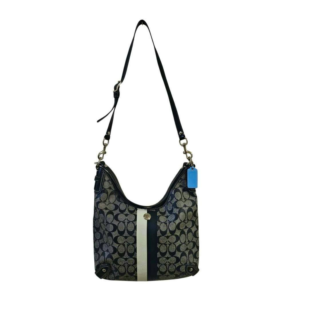 Front view of a black Coach 2-way shoulder handbag in canvas with repeating logo pattern, a vertical center stripe, adjustable shoulder strap, and a blue hangtag.