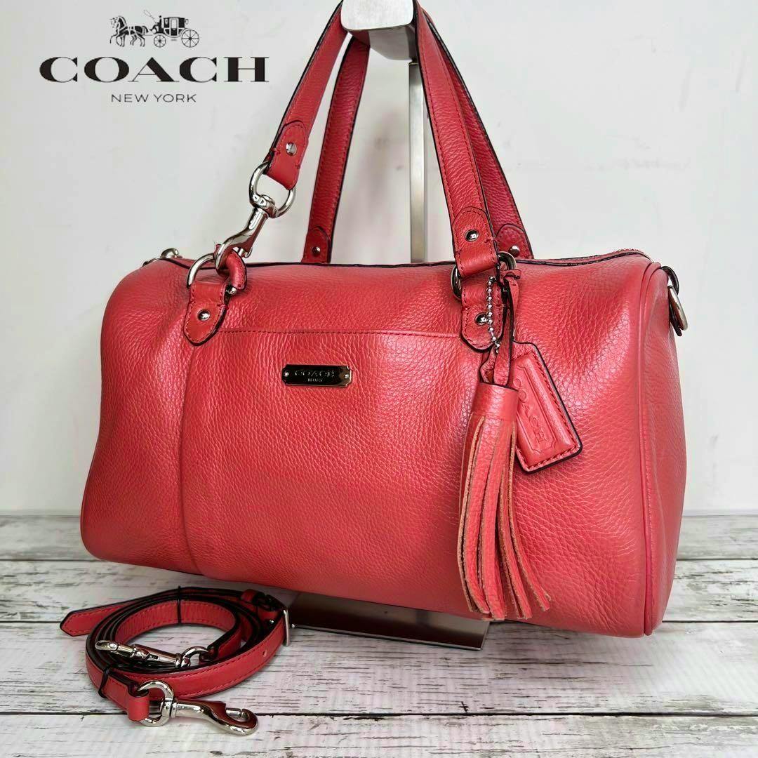 Red COACH leather 2-way handbag with tassel and detachable shoulder strap displayed on a stand.