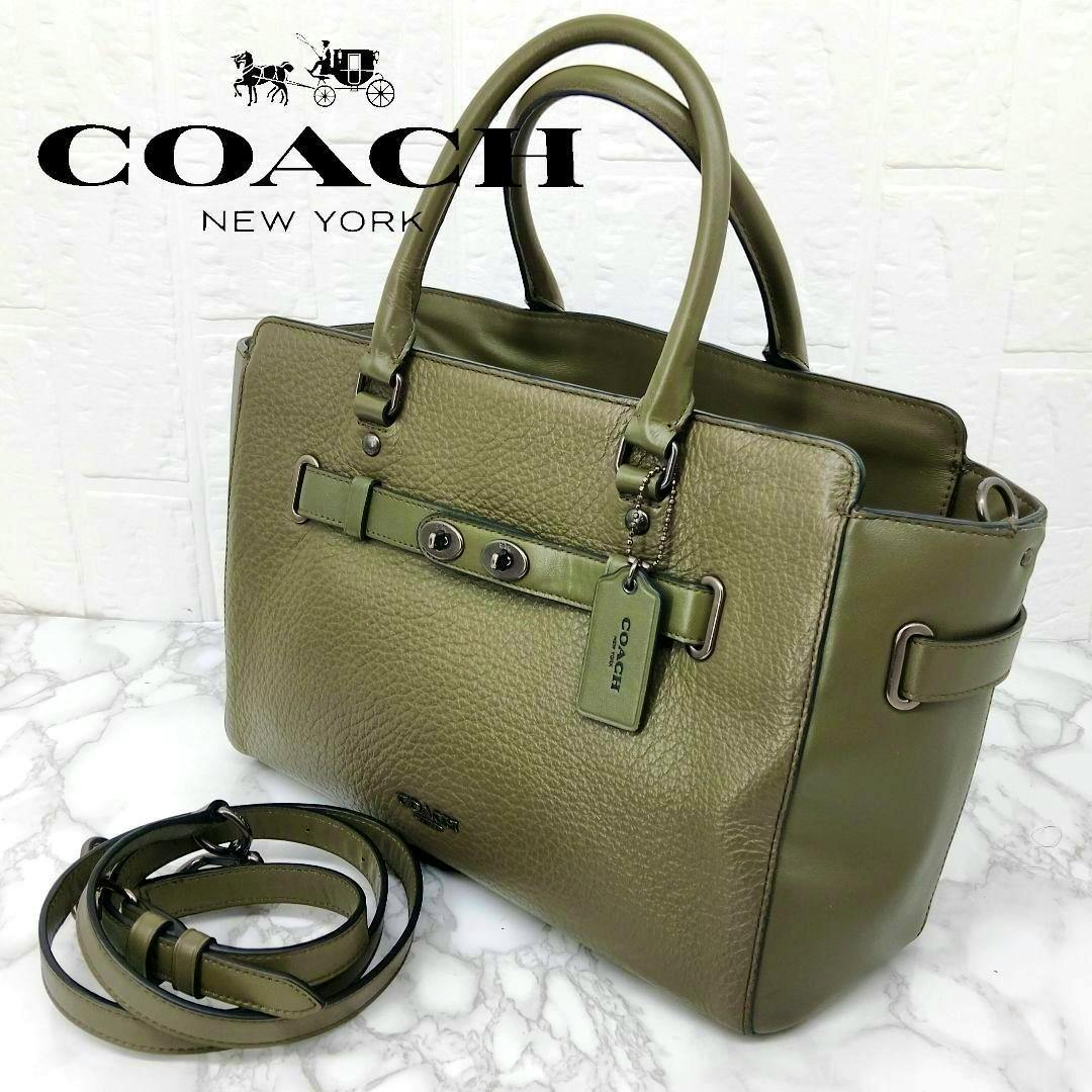 Olive-green Coach 2-way leather handbag with handles and a detachable shoulder strap on a marble surface.