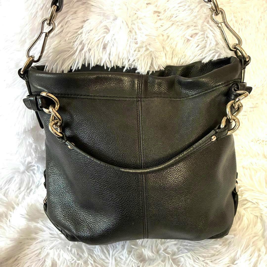 Front view of a black leather Coach one-shoulder bag with chain-link hardware on a white fur background.