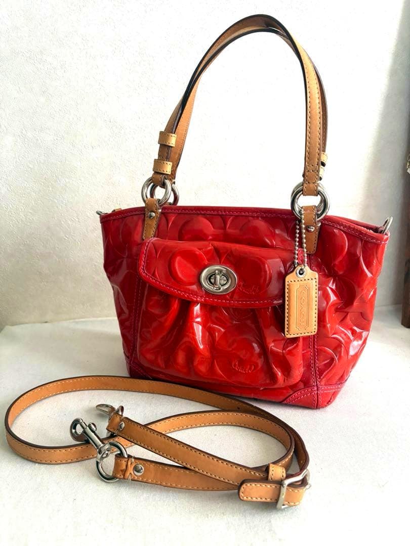 Red COACH patent leather 2way handbag with tan handles and a matching long shoulder strap placed in front.