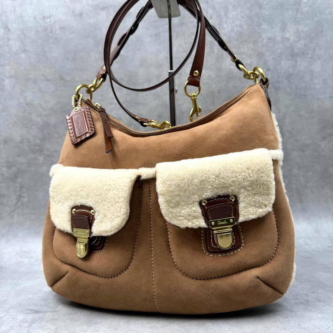 Front view of a brown Coach mouton 2-way shoulder bag with cream shearling pocket flaps and gold-tone hardware.