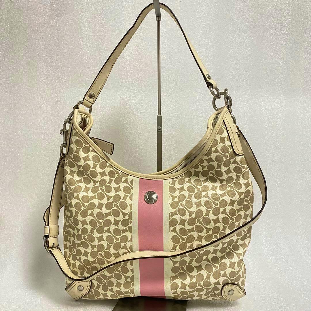 Front view of a beige Coach canvas 2-way shoulder bag with a central pink vertical stripe and leather straps.