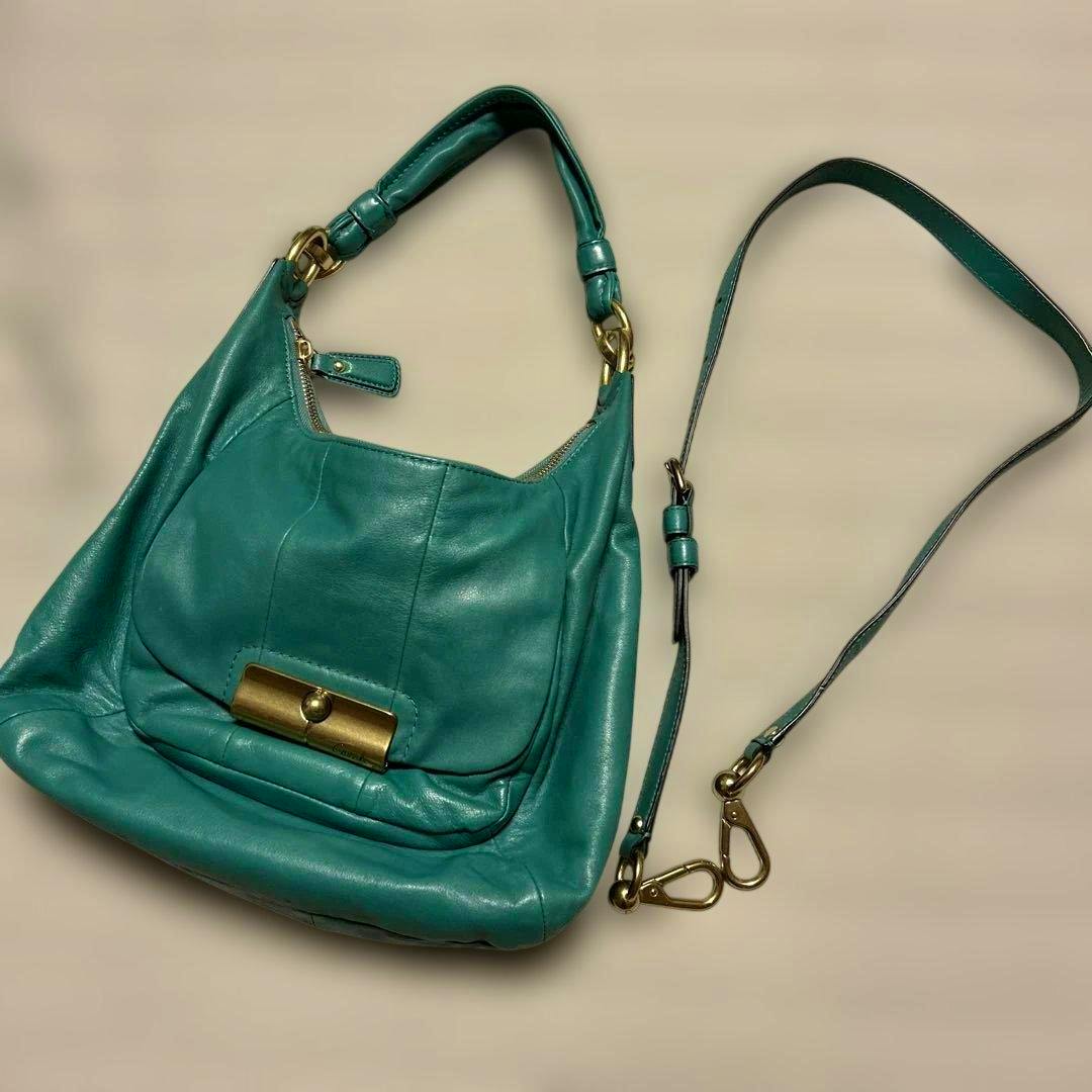 Turquoise blue Coach 2way shoulder bag with a short handle and detachable long strap laid flat.