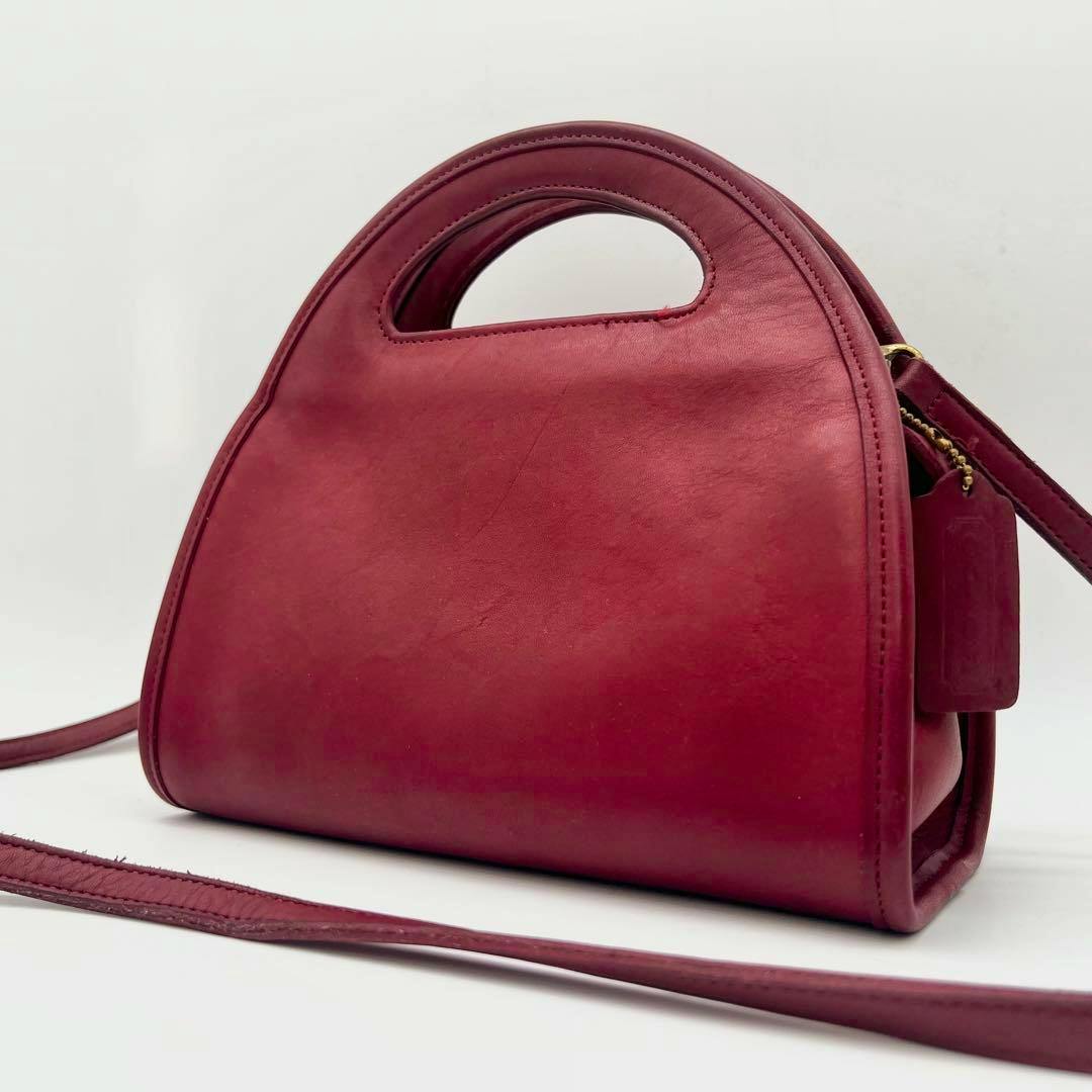 A red leather COACH 2Way half-moon shoulder handbag photographed at a three-quarter angle showing its top handle and long shoulder strap.