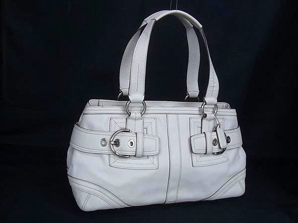 White COACH leather tote handbag with double top handles and front buckle details on a dark background.