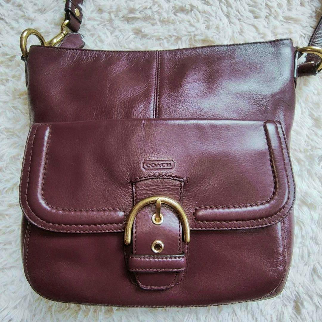 Front view of the burgundy Coach leather shoulder bag showing the front flap pocket with a gold-tone buckle.
