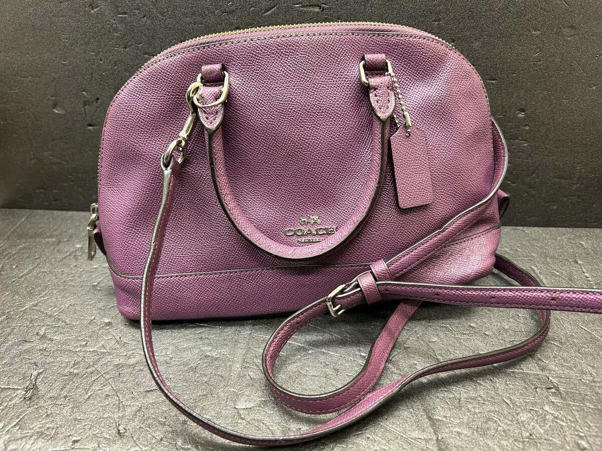 Front view of the COACH 2-way pink‑purple cow leather shoulder handbag showing handles, tag, and long strap.