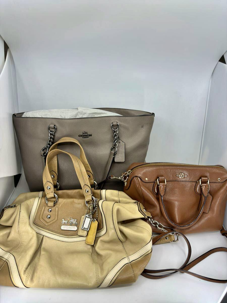 Three COACH bags — a gray tote, a beige handbag, and a brown leather shoulder bag — arranged on a white background.