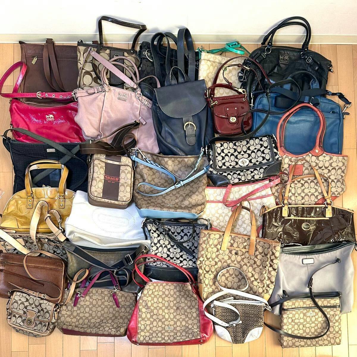 A collection of Coach bags and purses arranged on a wooden floor showing multiple signature 'C' canvas patterns and various tote, shoulder, and crossbody styles.