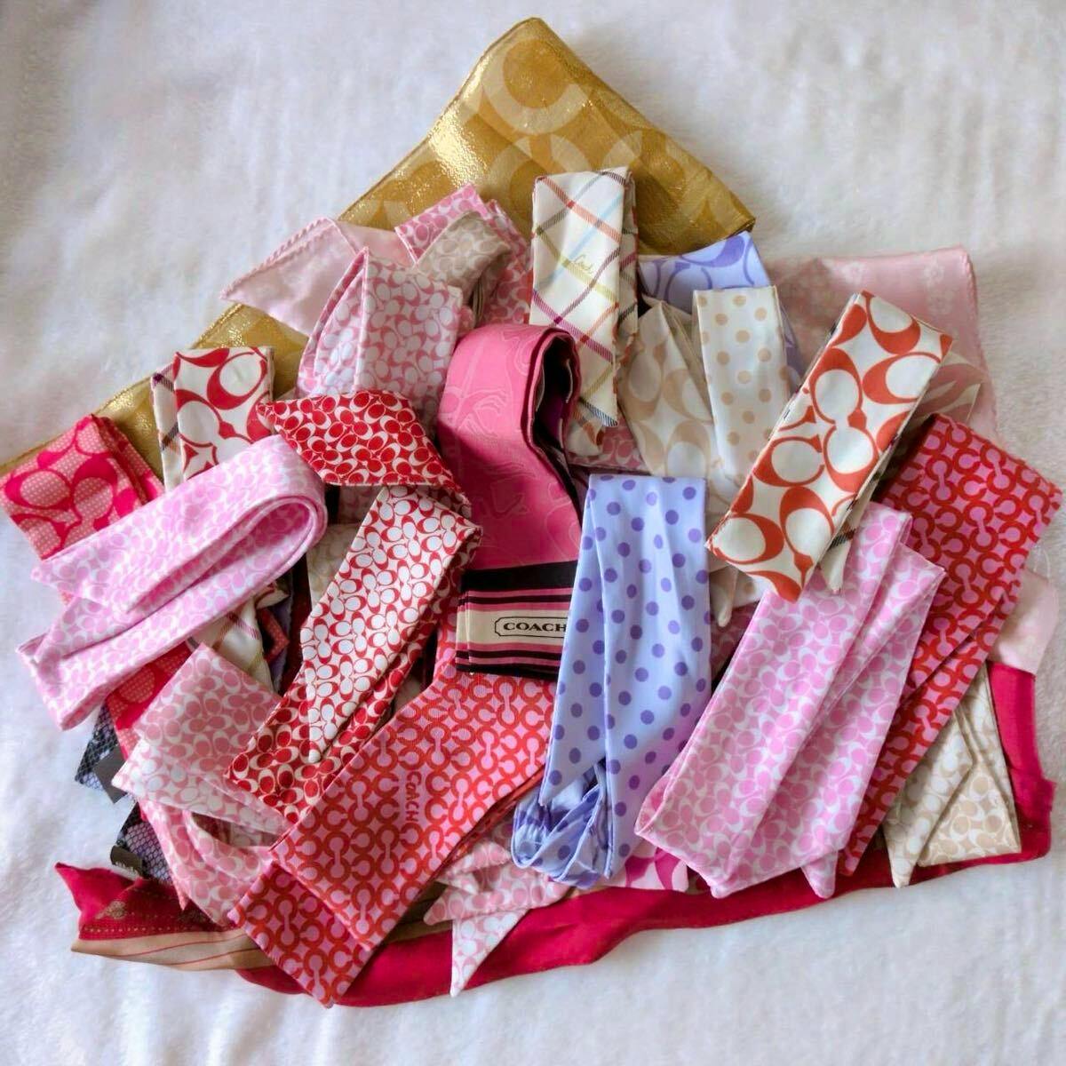 A pile of Coach ribbon-style and silk scarf pieces in various colors and patterns arranged on a flat surface.