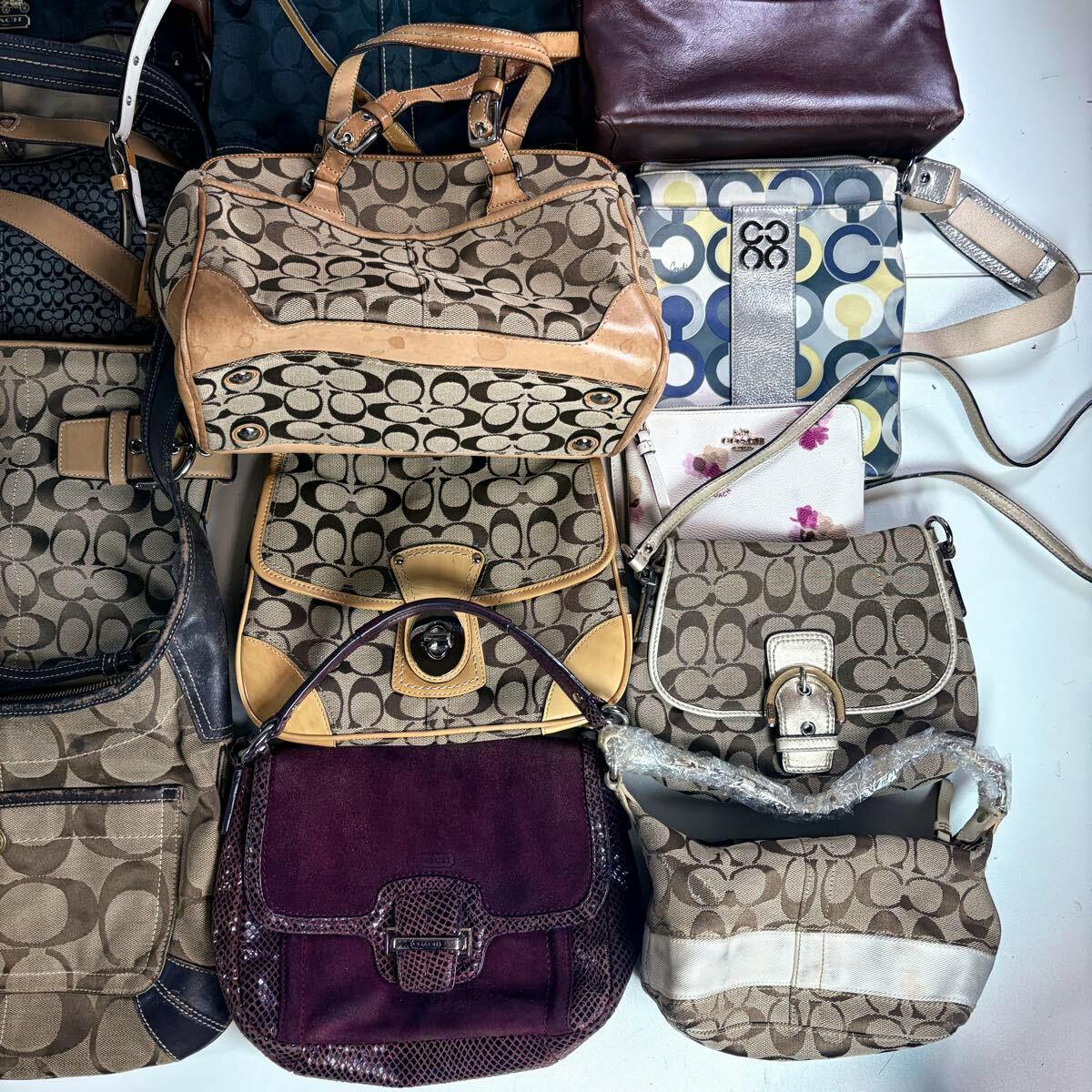 Top-down photo showing multiple Coach canvas and leather shoulder bags arranged together as a bulk set.