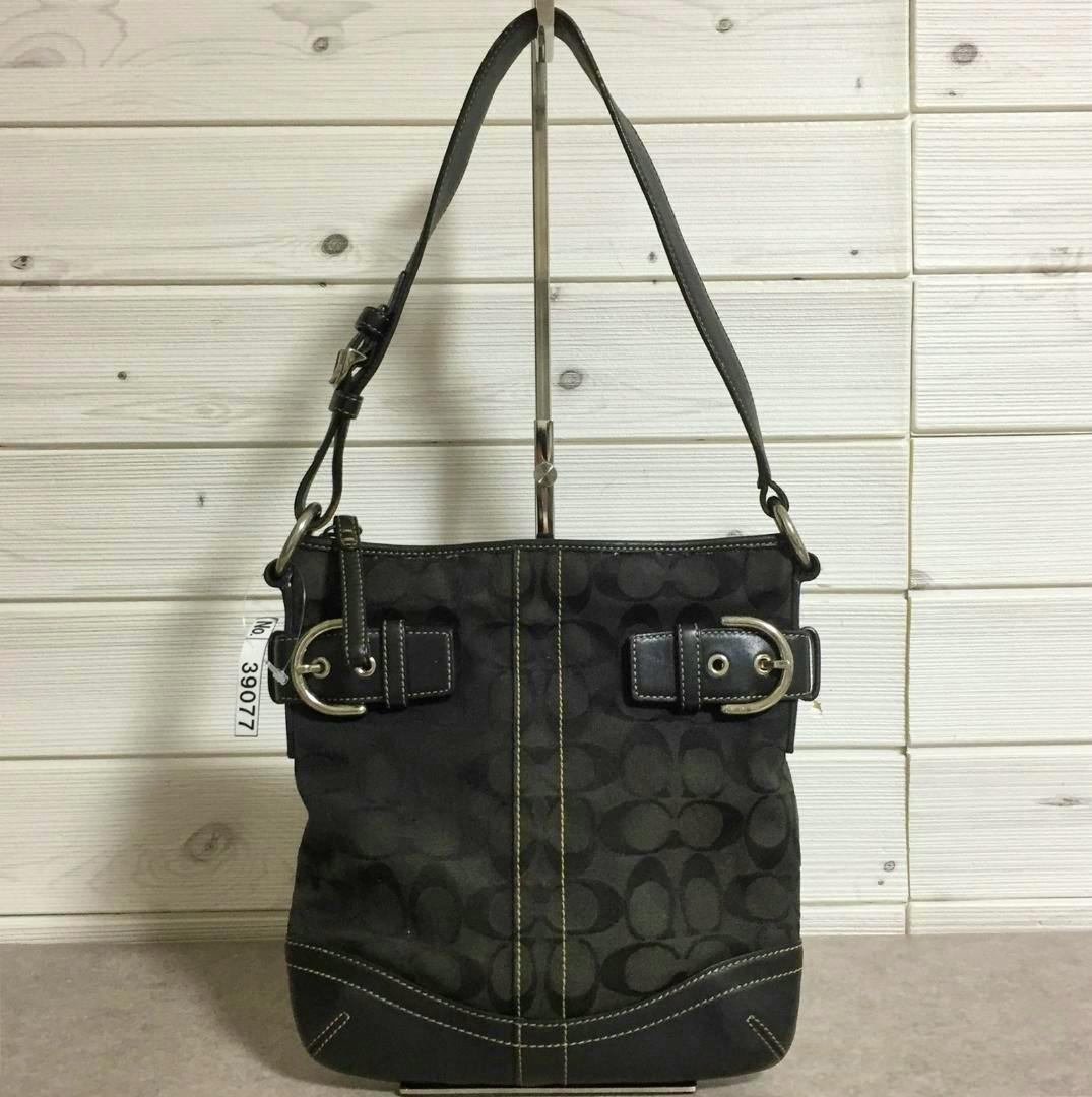 Front view of the Coach signature handbag in dark fabric with a single shoulder strap, buckle accents, and contrast stitching.
