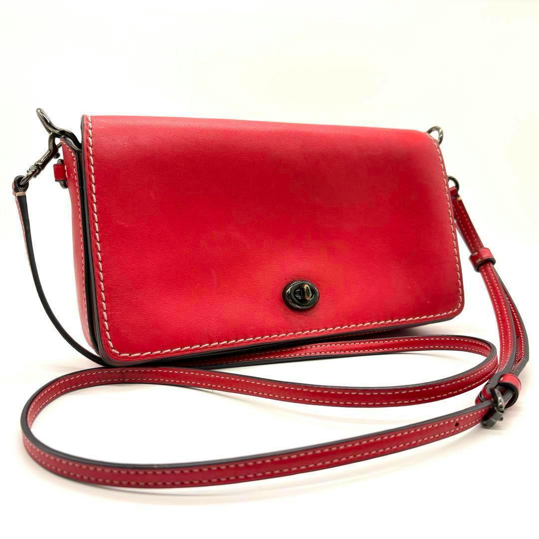Front view of a red Coach Dinky mini shoulder bag in cow leather with a turn-lock closure and long strap.