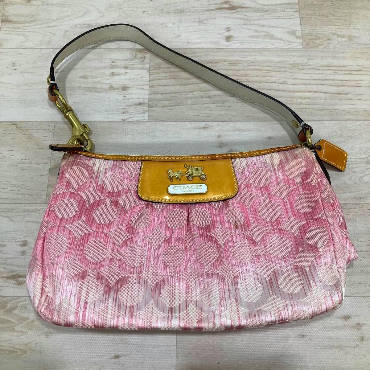 Front exterior of the COACH canvas and patent leather one-handle mini handbag in pink and yellow, laid flat on a light wood floor.
