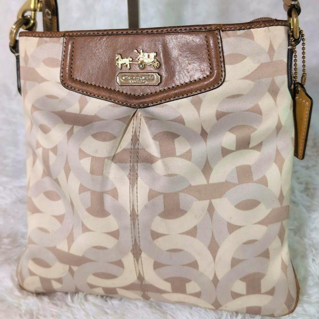 Front view of the COACH signature shoulder bag showing the horse-and-carriage logo, beige interlocking C pattern, and brown leather trim.
