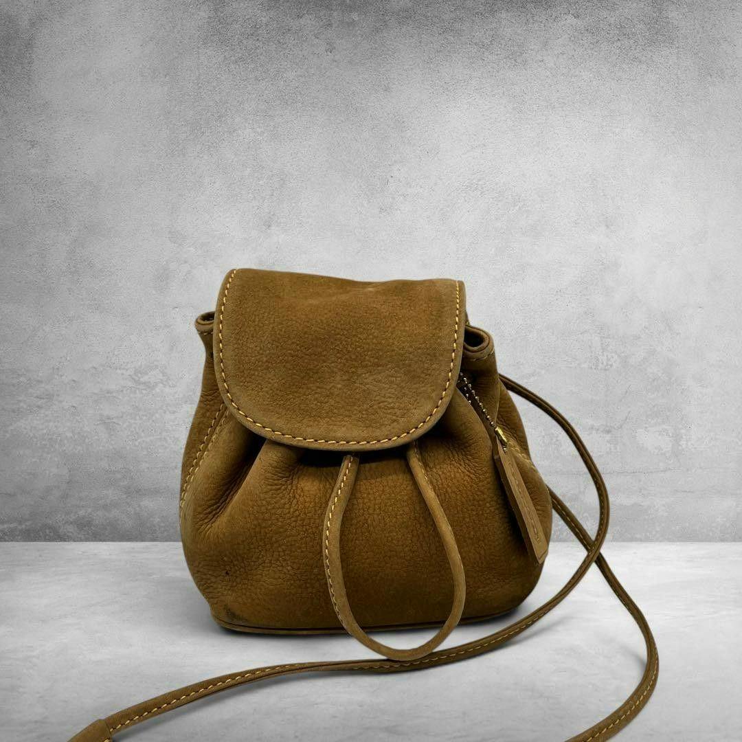 Front view of the Coach 4940 Nubuck drawstring bag showing the flap closure, drawstring cords, hanging tag, and long shoulder strap.