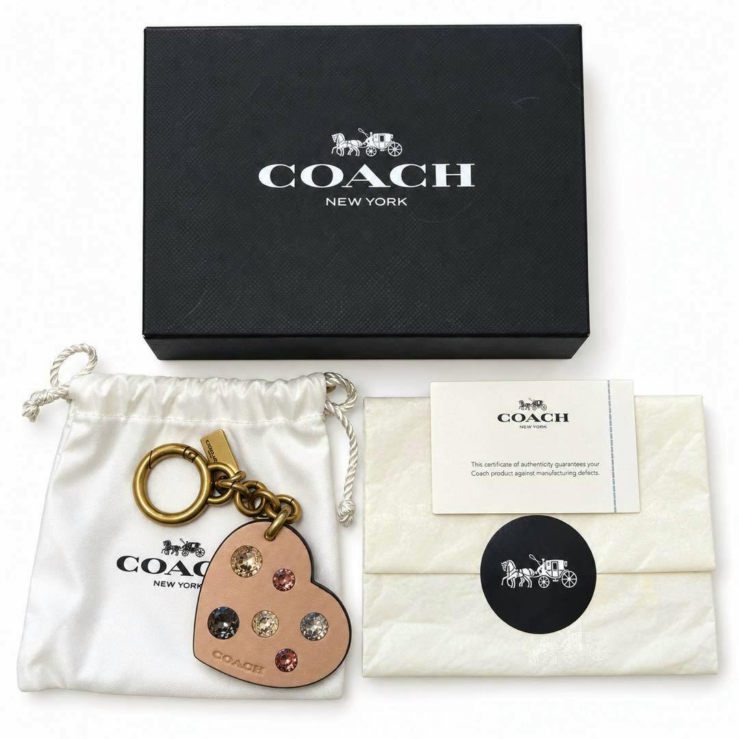 Heart-shaped Coach leather bag charm with multicolored crystal studs displayed with its Coach box, dust bag, and authenticity card.