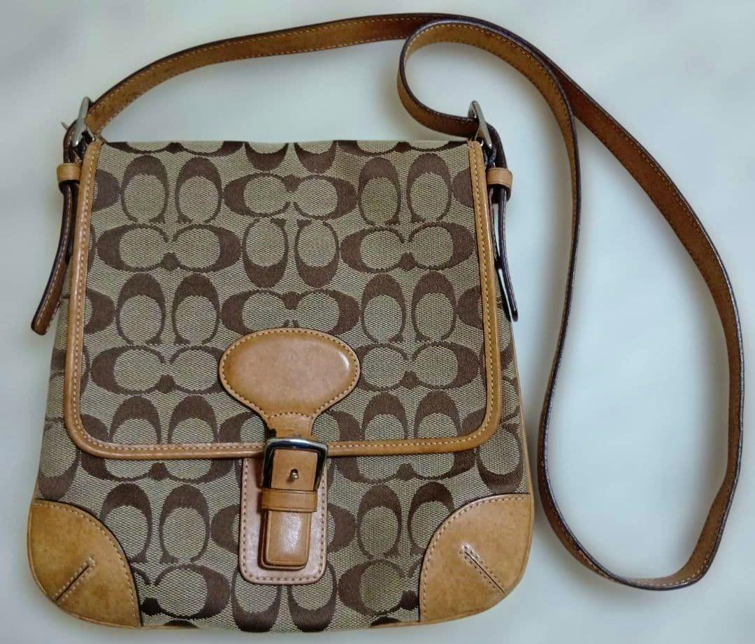 Front view of the Coach signature canvas shoulder bag showing the brown 'C' pattern, leather trim, buckle flap closure, and long shoulder strap.