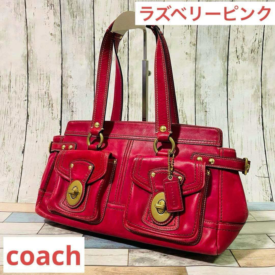 Pink Coach 65th Legacy Turn Lock cow leather handbag with two front pockets and gold turn-lock hardware, shown angled against a wood background.